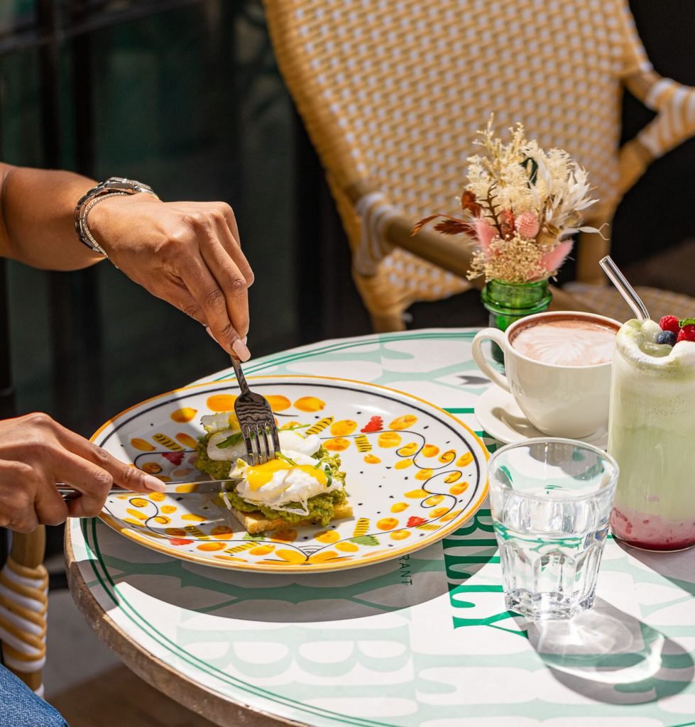Brunch Marrakech with avocado toast topped with poached eggs, served alongside matcha latte, hot chocolate, and fresh drinks on a sunny terrace
