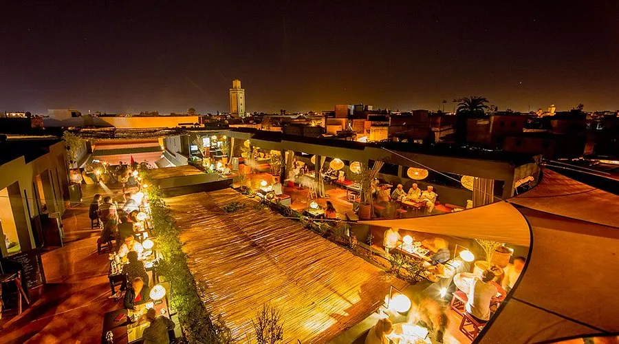 Terrasse rooftop animée la nuit à Marrakech avec vue sur le minaret et la médina
