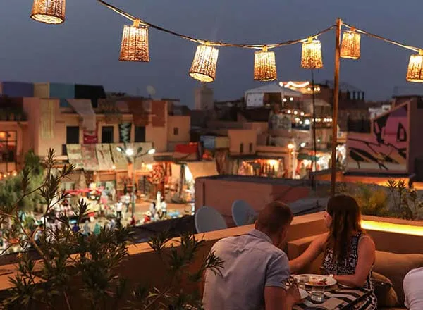 Couple dînant sur une terrasse rooftop avec vue sur la médina de Marrakech au crépuscule
